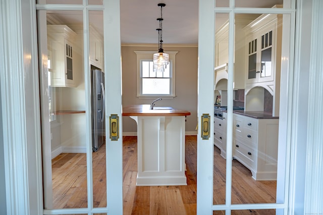 kitchen featuring stainless steel refrigerator with ice dispenser, light wood-type flooring, wood counters, glass insert cabinets, and pendant lighting