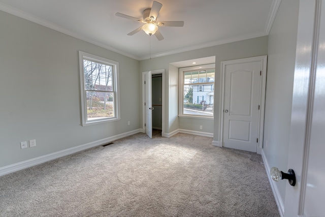 unfurnished bedroom featuring carpet, crown molding, multiple windows, baseboards, and ceiling fan