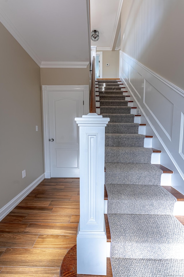 stairs featuring wood finished floors, crown molding, and a wainscoted wall