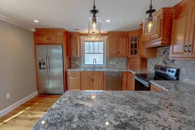 kitchen with appliances with stainless steel finishes, a sink, baseboards, crown molding, and light stone countertops