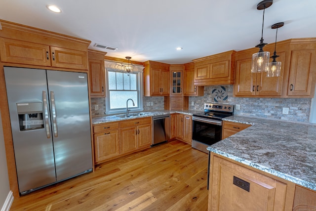 kitchen with appliances with stainless steel finishes, a sink, light wood-type flooring, light stone countertops, and recessed lighting