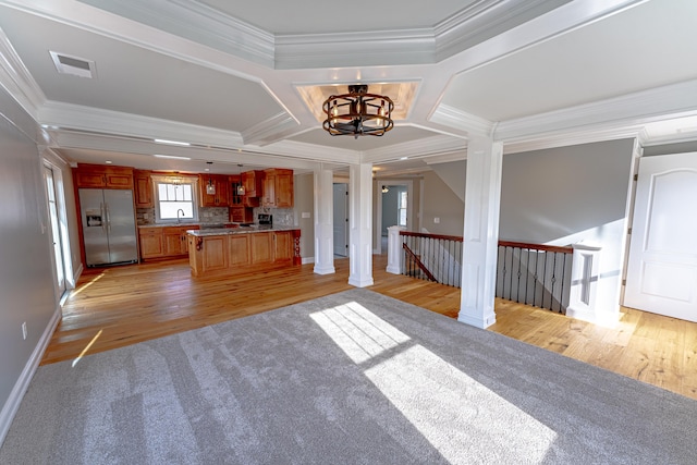 unfurnished living room with ornate columns, a chandelier, ornamental molding, and light wood-style floors