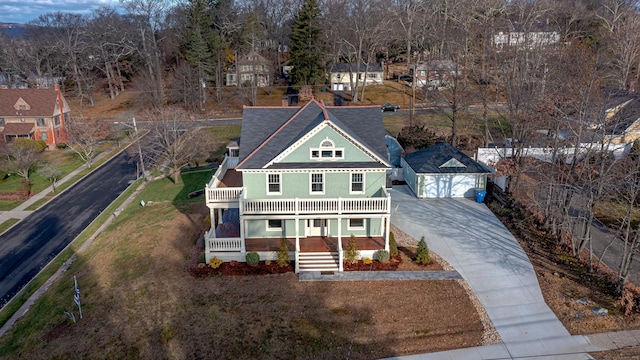 view of front facade with a porch, driveway, a detached garage, a balcony, and roof with shingles