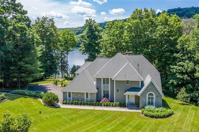 traditional home featuring stone siding, a front yard, and a chimney