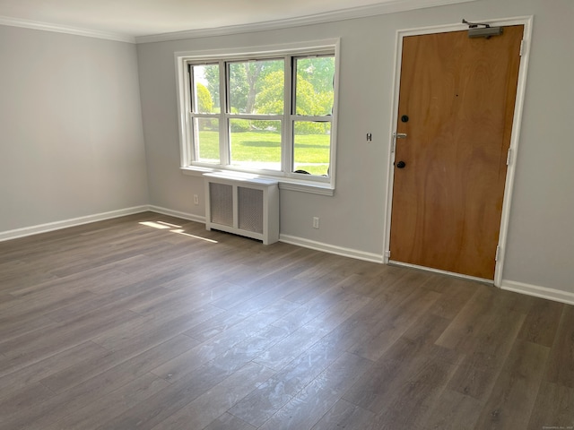 empty room with radiator heating unit, crown molding, baseboards, and dark wood finished floors