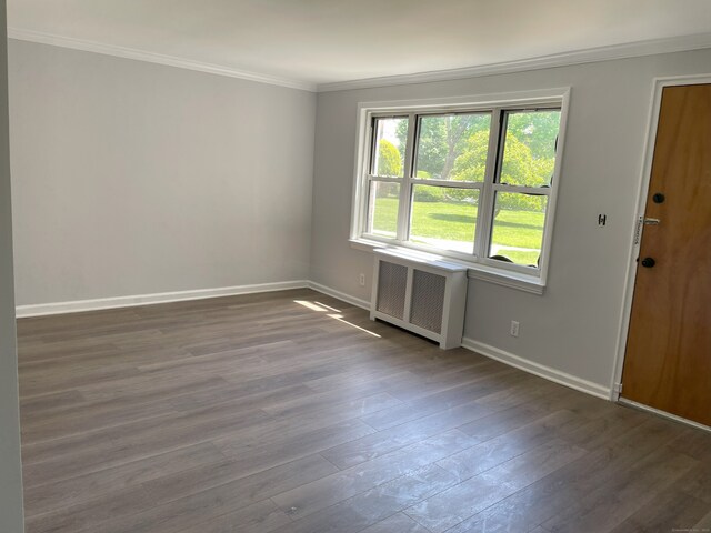 unfurnished room with radiator, dark wood-style flooring, crown molding, and baseboards