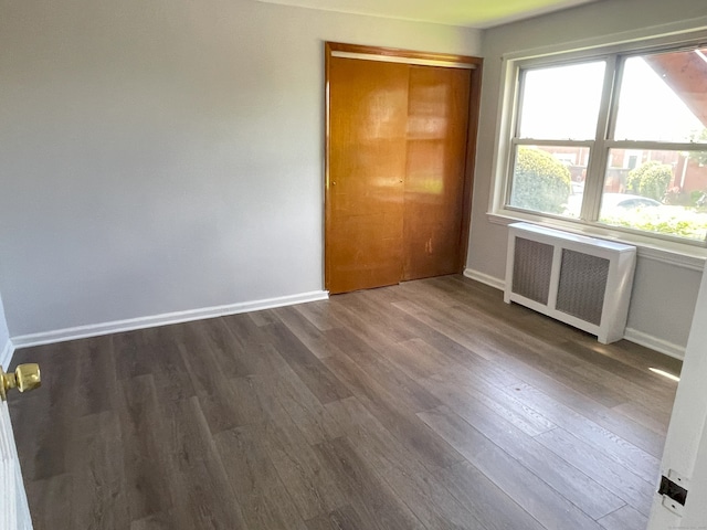 unfurnished bedroom featuring radiator, dark wood-type flooring, baseboards, and a closet