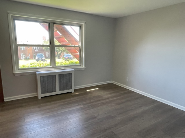 empty room with radiator, dark wood-type flooring, and baseboards