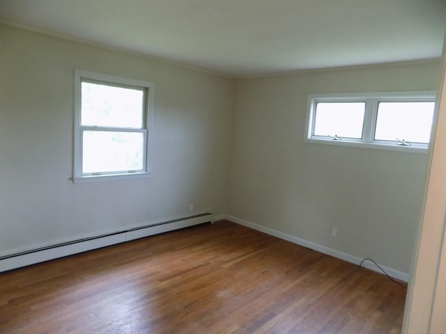 empty room with baseboard heating, wood finished floors, and baseboards