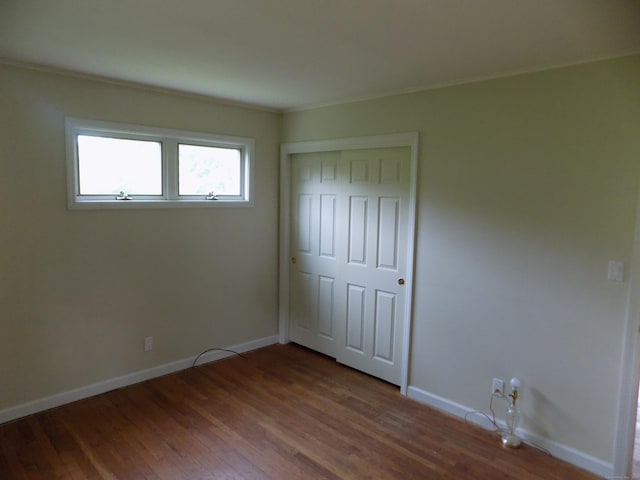 unfurnished bedroom with baseboards, dark wood-style floors, a closet, and ornamental molding