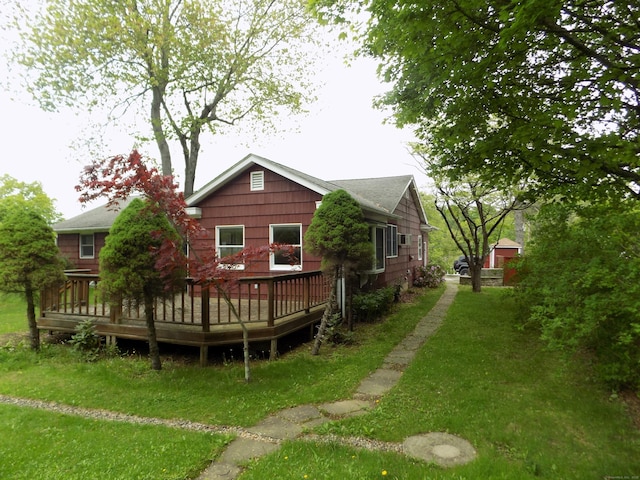 rear view of house featuring a deck, a shingled roof, and a lawn