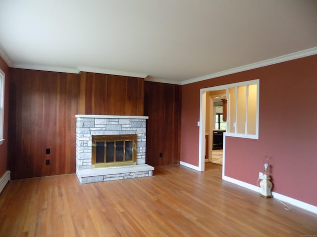unfurnished living room featuring wood finished floors, a stone fireplace, ornamental molding, baseboards, and a baseboard heating unit