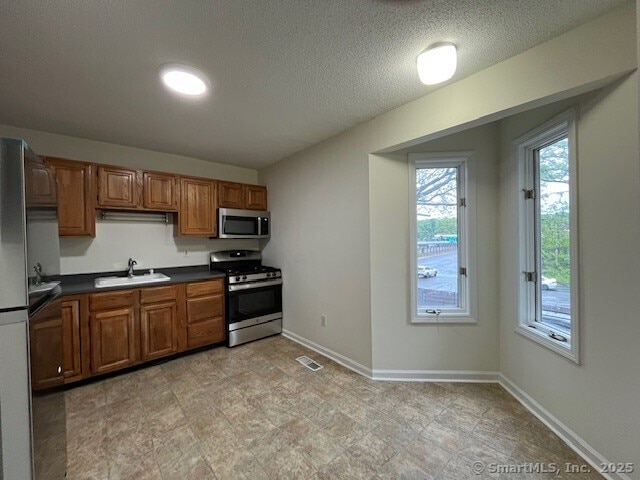 346 Prospect Ave Unit 3, New Haven, CT 06512 - kitchen with appliances with stainless steel finishes, a sink, dark countertops, brown cabinetry, and a textured ceiling