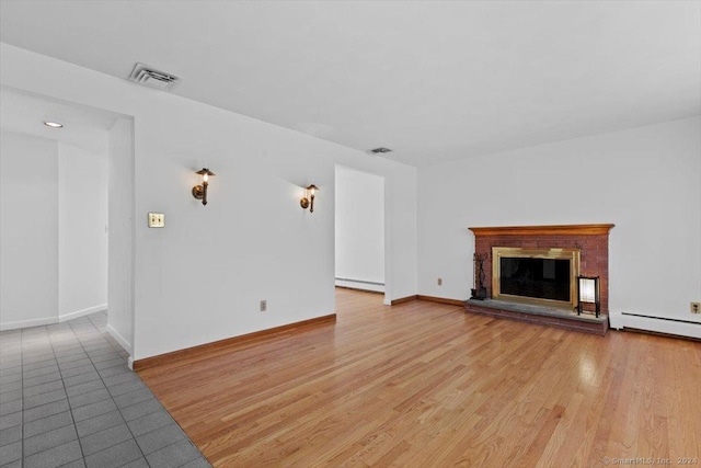 unfurnished living room featuring a baseboard radiator, a brick fireplace, wood finished floors, and baseboards