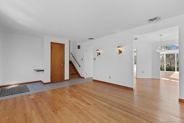 unfurnished living room featuring light wood-type flooring, a chandelier, stairs, and baseboards