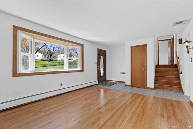 unfurnished living room featuring baseboard heating, wood finished floors, stairs, and baseboards