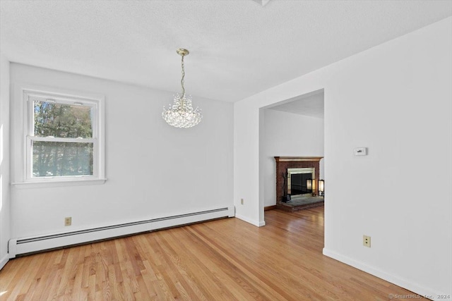unfurnished dining area with a baseboard heating unit, light wood finished floors, a chandelier, baseboards, and a fireplace
