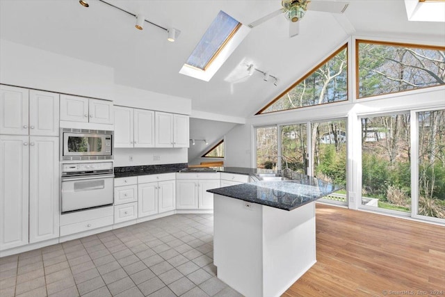 kitchen with rail lighting, appliances with stainless steel finishes, a skylight, a sink, and a peninsula