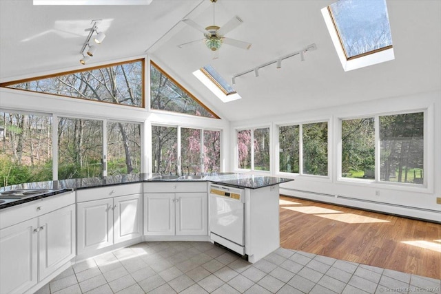unfurnished sunroom with track lighting, a skylight, lofted ceiling, a baseboard radiator, and a sink