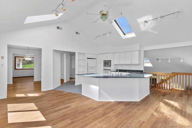 kitchen featuring rail lighting, a skylight, white appliances, ceiling fan, and light wood finished floors