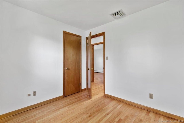 spare room with baseboards, light wood-type flooring, and a baseboard radiator