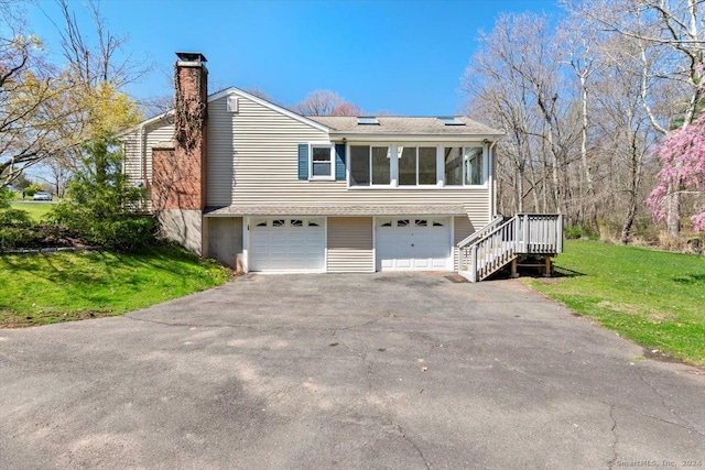 view of front of house featuring asphalt driveway, a chimney, an attached garage, a front lawn, and stairway
