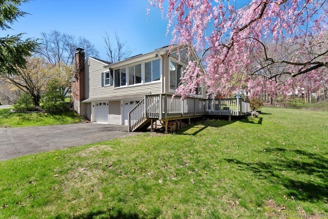 view of front of house with a garage, asphalt driveway, a deck, a chimney, and a front yard