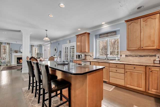 kitchen featuring a sink, ornamental molding, a breakfast bar area, dishwashing machine, and light wood-style flooring