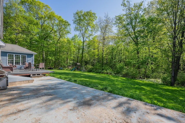 view of patio with a wooden deck, a playground, and a forest view