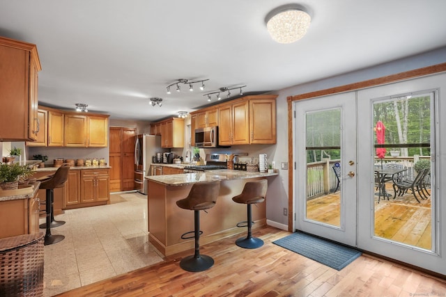 387 New London Tpke, Stonington, CT 06378 - kitchen featuring appliances with stainless steel finishes, a peninsula, french doors, a kitchen bar, and light wood-type flooring