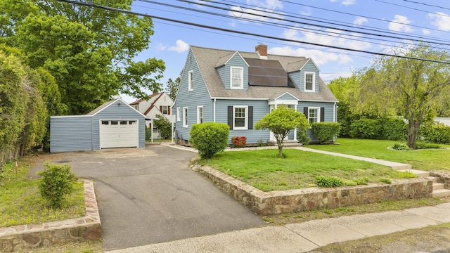 cape cod-style house featuring an outbuilding, driveway, a detached garage, a front yard, and a chimney