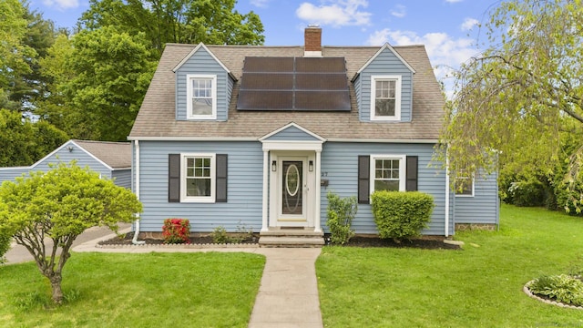 view of front of home featuring a front lawn, solar panels, a shingled roof, and a chimney