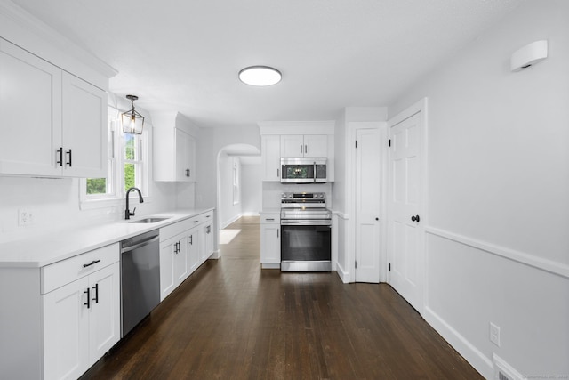 kitchen with appliances with stainless steel finishes, a sink, dark wood-type flooring, light countertops, and white cabinetry