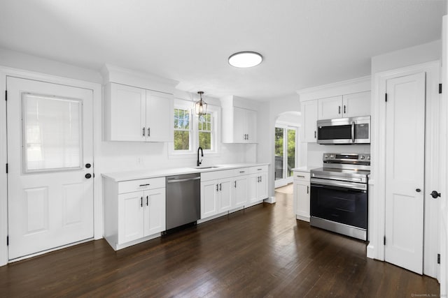 kitchen with stainless steel appliances, a sink, arched walkways, dark wood-style floors, and light countertops