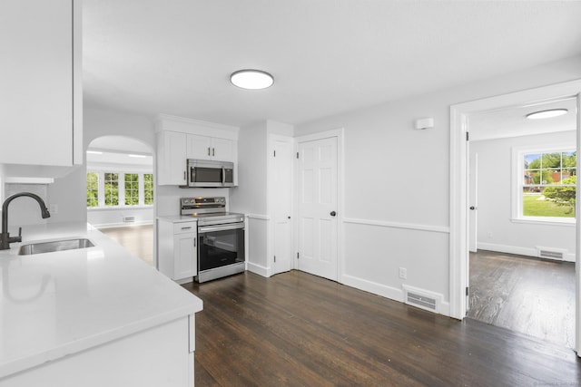 kitchen with appliances with stainless steel finishes, a sink, dark wood-style floors, light countertops, and white cabinetry