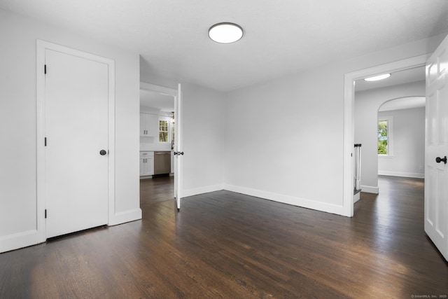 empty room with arched walkways, dark wood-type flooring, and baseboards