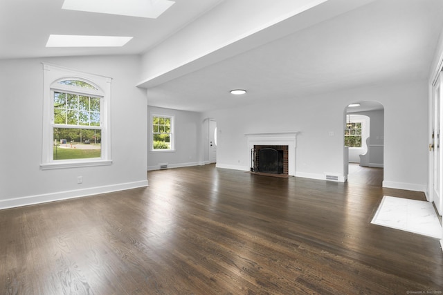 unfurnished living room with arched walkways, a fireplace, dark wood-style floors, a skylight, and lofted ceiling