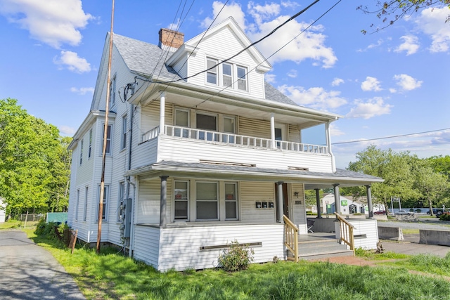 view of front of house with covered porch, a balcony, a chimney, and roof with shingles