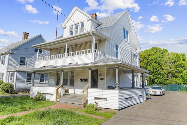 view of front of home featuring covered porch, a balcony, a chimney, and roof with shingles