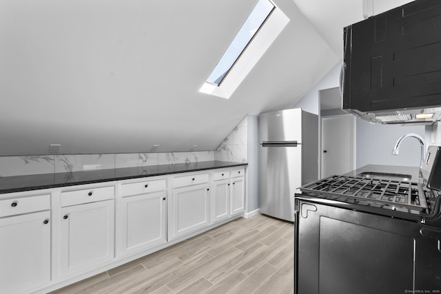 kitchen with a skylight, freestanding refrigerator, white cabinetry, lofted ceiling, and light wood finished floors