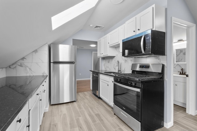 kitchen with appliances with stainless steel finishes, a skylight, vaulted ceiling, a sink, and tasteful backsplash