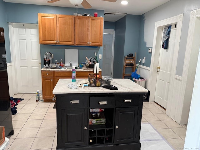 kitchen with a ceiling fan, light tile patterned floors, dark cabinets, a center island, and brown cabinets