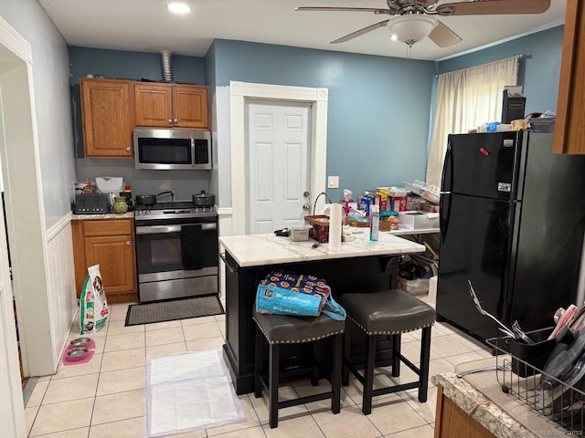 kitchen featuring appliances with stainless steel finishes, ceiling fan, light tile patterned floors, light countertops, and brown cabinets