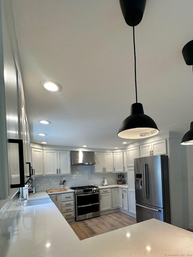 kitchen featuring appliances with stainless steel finishes, wall chimney range hood, a sink, light wood-style floors, and hanging light fixtures