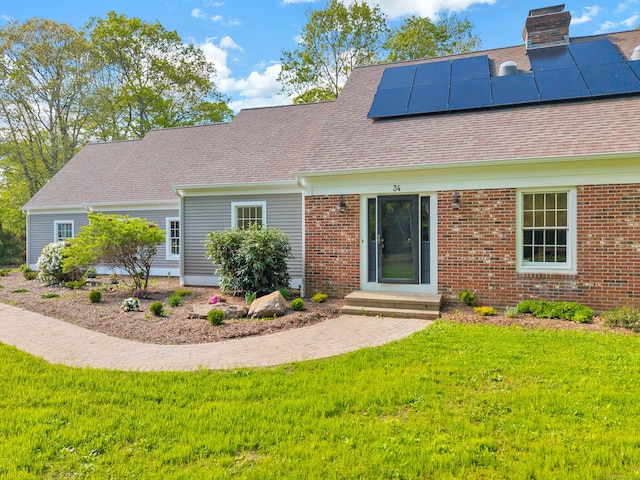 34 Willow Ln, East Lyme, CT 06333 - view of front facade featuring a front yard, roof mounted solar panels, a shingled roof, a chimney, and brick siding