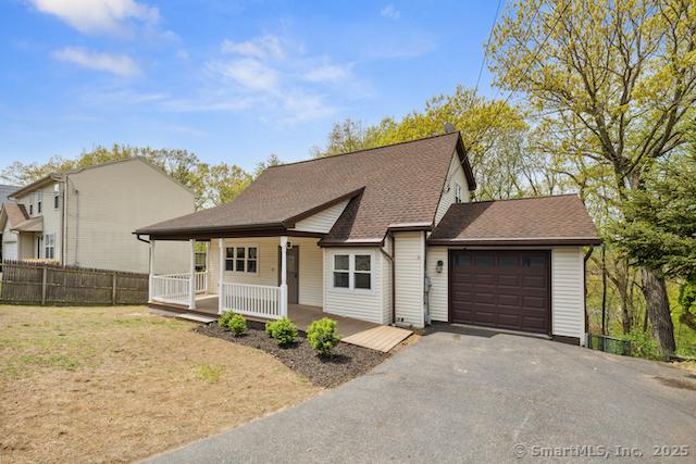 view of front facade featuring an attached garage, a porch, driveway, fence, and roof with shingles