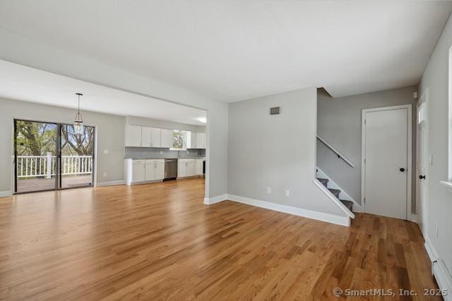unfurnished living room featuring light wood-type flooring, baseboards, and stairs