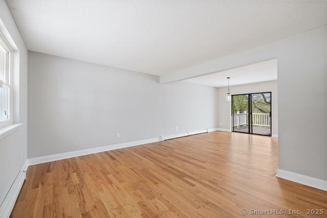empty room featuring light wood-style flooring, baseboard heating, and baseboards