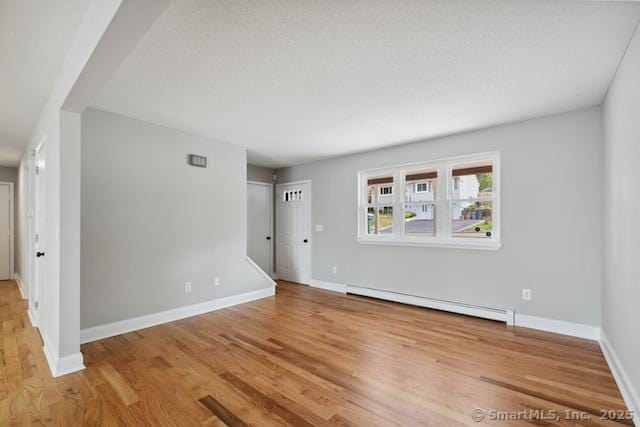 unfurnished living room with baseboard heating, wood finished floors, and baseboards
