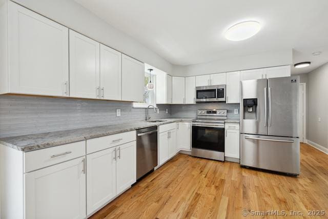 kitchen featuring appliances with stainless steel finishes, decorative backsplash, white cabinetry, a sink, and light wood-type flooring
